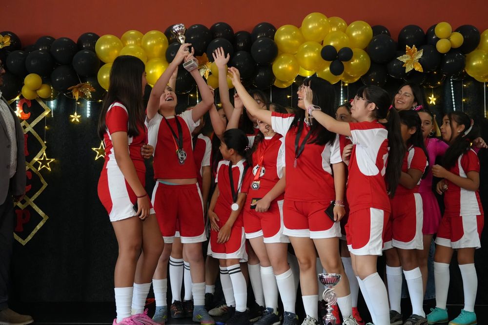 Equipo de fútbol femenino del colegio celebrando con medallas y trofeo